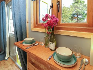 A wooden dining counter with two place settings flowers in a glass vase and a wine bottle by a window at Tower Hut in Ryde