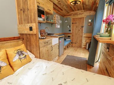 A wooden interior room with a kitchen area a bed with bee pillows a small dining shelf and a wooden door at Tower Hut in Ryde