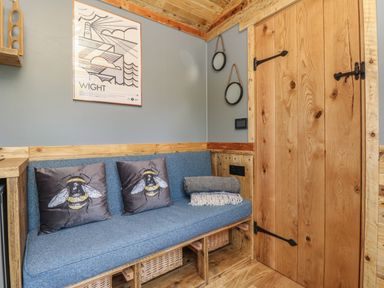 A small sitting area with a blue cushioned bench with two bee-themed pillows and a folded blanket beside a wooden door at Tower Hut in Ryde