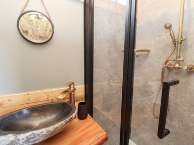 A bathroom with a stone sink wooden countertop round mirror and a glass door shower at Tower Hut in Ryde