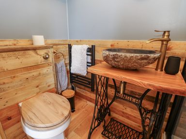A bathroom with a wooden toilet seat a stone sink on a wooden table with a vintage sewing machine base at Tower Hut in Ryde