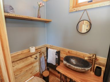 A small bathroom with a stone sink on a wooden counter and a round mirror hanging on the wall at Tower Hut in Ryde