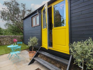 An outdoor patio with a blue table and two chairs a potted plant yellow double doors on a dark wooden structure at Tower Hut in Ryde