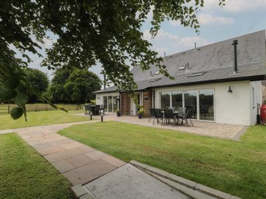 A garden patio area with tables and chairs outside a house with large windows at Primrose Cottage in Brendon Hill near Roadwater