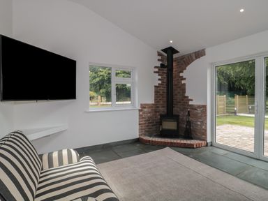 A living room with a striped sofa a wall-mounted television a brick fireplace and glass doors at Primrose Cottage in Brendon Hill near Roadwater