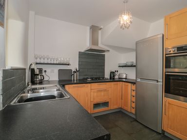 A kitchen with wooden cabinets black countertops a stainless steel refrigerator oven and a double sink at Primrose Cottage in Brendon Hill near Roadwater