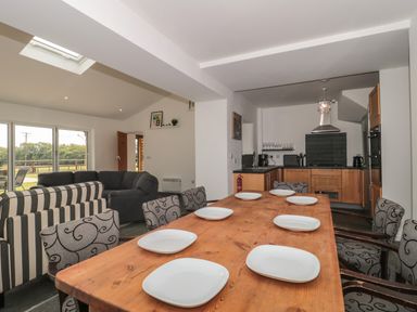 A dining area with a wooden table set with plates and chairs next to a kitchen with wooden cabinets and a living room with sofas at Primrose Cottage in Brendon Hill near Roadwater