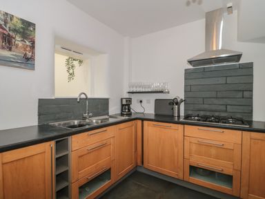 A kitchen with wooden cabinets black countertops a double sink a gas stove a coffee maker and glasses on a shelf at Primrose Cottage in Brendon Hill near Roadwater