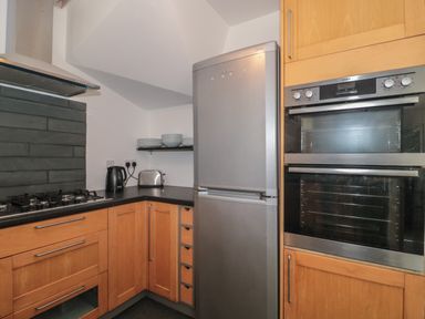 A kitchen with wooden cabinets a silver refrigerator an oven and countertop appliances at Primrose Cottage in Brendon Hill near Roadwater