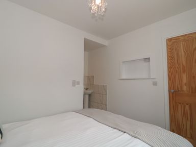 A bedroom with a bed a wooden door a small sink area and a small recessed shelf at Primrose Cottage in Brendon Hill near Roadwater