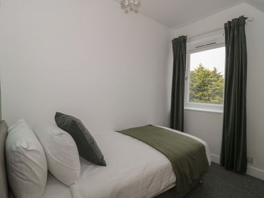 A bedroom with a bed near a window with green curtains at Primrose Cottage in Brendon Hill near Roadwater