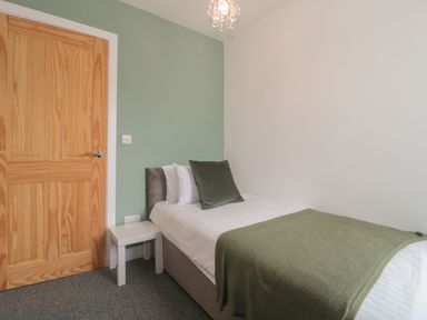 A bedroom with a single bed green blanket and cushion a wooden door and a small white table at Primrose Cottage Brendon Hill near Roadwater