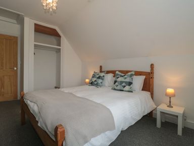 A bedroom with a wooden bed, patterned pillows, bedside table with lamp and an open closet at Primrose Cottage Brendon Hill near Roadwater