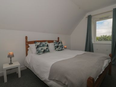 A bedroom with a wooden double bed two patterned pillows bedside tables with lamps and a window with curtains at Primrose Cottage in Brendon Hill near Roadwater