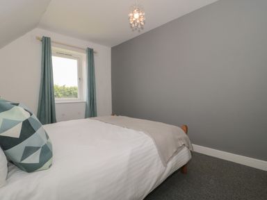 A bedroom with a bed white bedding geometric pillows gray walls and a window with curtains at Primrose Cottage in Brendon Hill near Roadwater