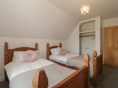 A bedroom with two wooden single beds and an open wardrobe at Primrose Cottage in Brendon Hill near Roadwater