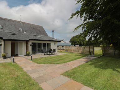A garden with a stone patio and outdoor dining set beside a house with a grey roof and white walls at Primrose Cottage in Brendon Hill near Roadwater
