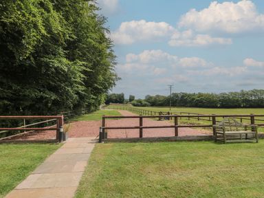 A fenced gravel path with grass and trees on the side and a bench at Primrose Cottage in Brendon Hill near Roadwater