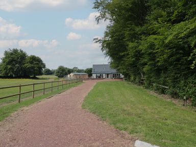 A gravel driveway leading to a house with a slate roof surrounded by trees and grassy fields at Primrose Cottage in Brendon Hill near Roadwater