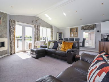 A living room with leather sofas pillows and patio doors overlooking water at Capenwray in Carnforth
