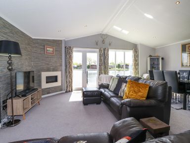 A living room with leather sofas a TV and fireplace next to glass doors leading outside at Capenwray in Carnforth