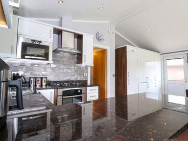 A kitchen with white cabinets a microwave oven a stove a coffee maker and a countertop at Capenwray in Carnforth