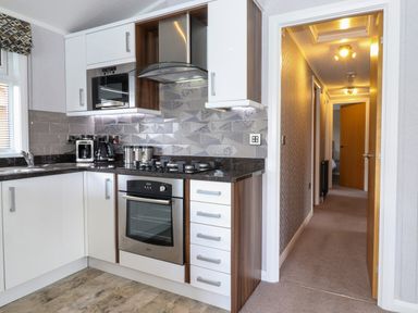A kitchen with white cabinets a gas stove and oven a coffee maker and a hallway with doors at Capenwray in Carnforth