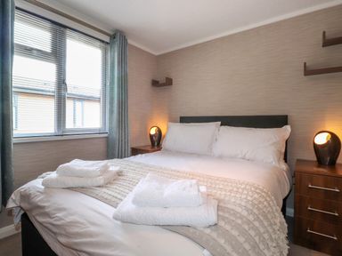 A bedroom with a bed made with white linens and towels on top two bedside tables with lamps and a window with curtains at Capenwray in Carnforth