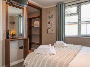 A bedroom with a bed folded towels on it a wall mirror a shelves with towels and a window with blinds and curtains at Capenwray in Carnforth