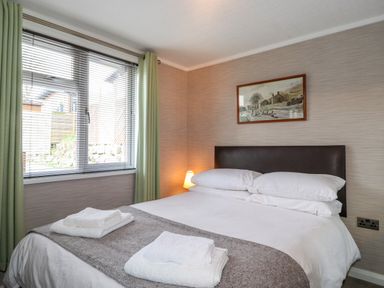 A bedroom with a bed linens towels a window with blinds and curtains and a framed picture on the wall at Capenwray in Carnforth