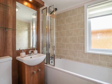 A bathroom with a sink cabinet toilet bathtub shower and window at Capenwray Carnforth