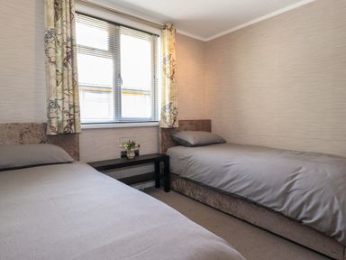 A bedroom with two single beds a window with curtains and a small black table with flowers between the beds at Capenwray in Carnforth