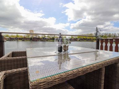 A glass top wicker table with wine and glasses on a balcony overlooking a lake with houses in the background at Capenwray in Carnforth