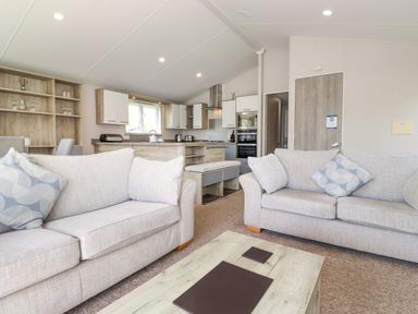 A living room with two sofas and a coffee table open to a kitchen with cabinets and appliances at Coniston in Carnforth