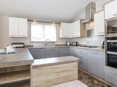 A kitchen with grey and white cabinets a gas stove oven toaster kettle and a window at Coniston in Carnforth