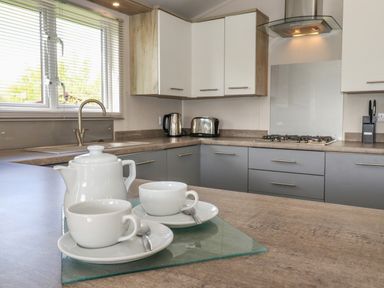A kitchen with a teapot and two cups on a countertop near a sink stove and cabinets at Coniston in Carnforth