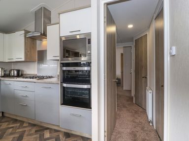 A kitchen with cabinets a built in microwave oven stove and a hallway with doors and carpet at Coniston in Carnforth