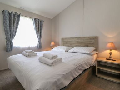 A bedroom with a double bed with white linens folded towels bedside table and lamp at Coniston in Carnforth