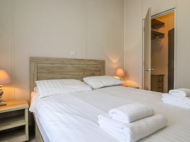 A bedroom with a wooden bed with white linens and pillows two bedside tables with lamps an open door showing a walk-in closet with shelves and drawers at Coniston in Carnforth