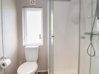 A bathroom with a toilet next to a window and a glass enclosed shower at Coniston in Carnforth