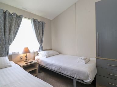 A bedroom with two single beds a bedside table with a lamp and curtains at Coniston in Carnforth