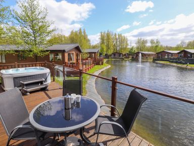 A patio with table and chairs overlooking a pond with fountain and cabins at Coniston in Carnforth