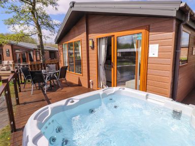 An outdoor deck with a hot tub a table and chairs outside wooden cabins at Coniston in Carnforth