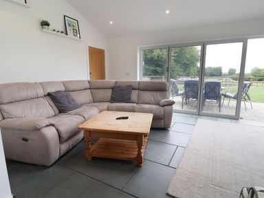 A living room with a gray sectional sofa wooden coffee table and sliding glass doors opening to an outdoor patio at Campion Cottage in Brendon Hill near Roadwater