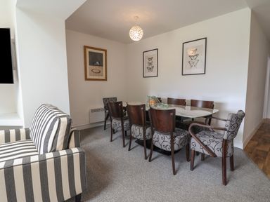A dining room with a marble table surrounded by upholstered chairs and a striped armchair at Campion Cottage in Brendon Hill near Roadwater