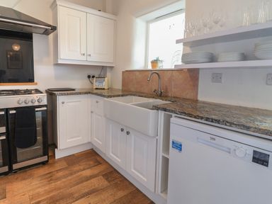 A kitchen with stove sink dishwasher shelves with dishes and wooden floor at Campion Cottage in Brendon Hill near Roadwater