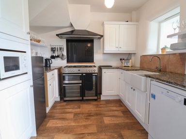 A kitchen with white cabinets wooden floor and stainless steel appliances at Campion Cottage in Brendon Hill near Roadwater