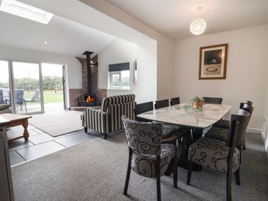 A dining area with a marble table and patterned chairs next to a living room with striped armchairs and a wood stove at Campion Cottage in Brendon Hill near Roadwater