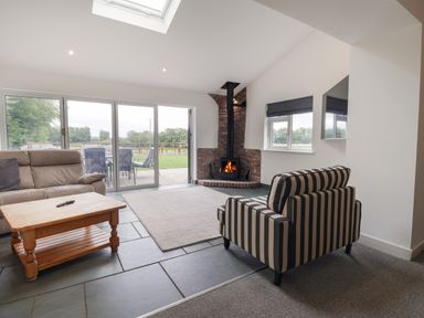 A living room with a wood stove fireplace sofa striped armchair wooden coffee table and glass doors leading outside at Campion Cottage Brendon Hill near Roadwater