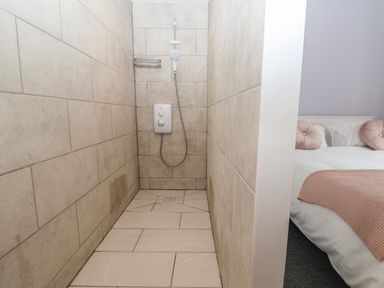 A tiled shower area with a white shower unit and a bed with pink cushions and a blanket at Campion Cottage in Brendon Hill near Roadwater